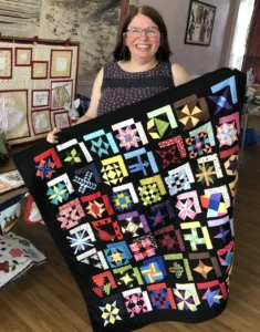 Claire from “Thistle” in Cowplain showing a quilt with a black background, adorned with a patchwork of multicoloured squares.