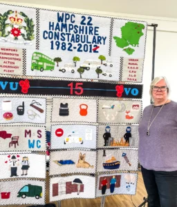 Jackie Dimmock stands next to her quilted work, sharing insights from her career as a policewoman during her talk.