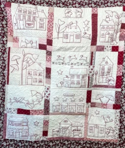 Red and white quilt with houses, cats and dogs on