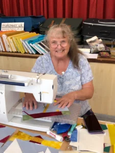 Jan Allston sitting at her sewing machine, surrounded by different fabrics and sewing items.